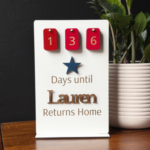 Countdown sign with red number tiles and a blue star, placed on a dark surface with a plant in the background.