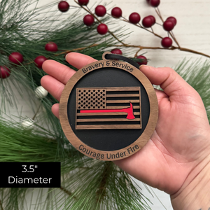 Hand holding a wooden ornament with American flag design and text, surrounded by greenery and berries.