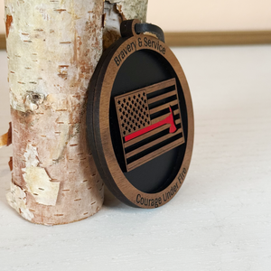 Wooden pendant with American flag design and engraved text, leaning against a tree trunk.