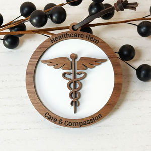 Wooden ornament with caduceus symbol and 'Healthcare Hero Care & Compassion' text on a white background.