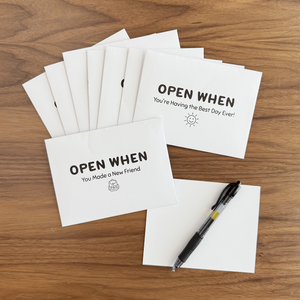 Set of 'Open When' cards on a wooden surface with a pen.