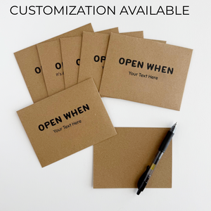 Kraft paper cards with 'Open When' text, customizable with a pen on a white background.