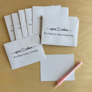 Set of white cards with humorous text on a wooden surface with a pink pen.