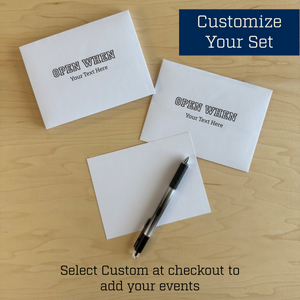 Two white envelopes and one card with 'Open When' text on a wooden surface, accompanied by a pen.