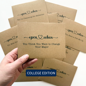 Kraft paper card with open when text held by a hand, surrounded by more cards on a white background.