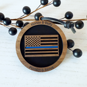 Wooden ornament with American flag design, 'Honor & Duty' and 'Protect & Serve' text, on a white background with black berries.