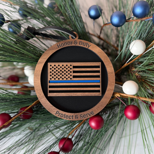 Wooden ornament with American flag design and text 'Honor & Duty', 'Protect & Serve' on a Christmas tree background.