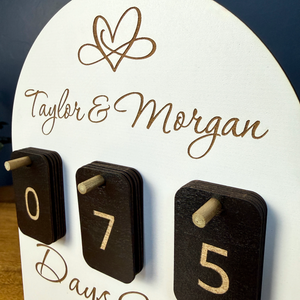 Close-up of personalized wedding countdown sign with engraved couple names and black number tiles