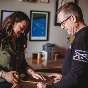 Two people working together on a project in a room with framed pictures on the wall.